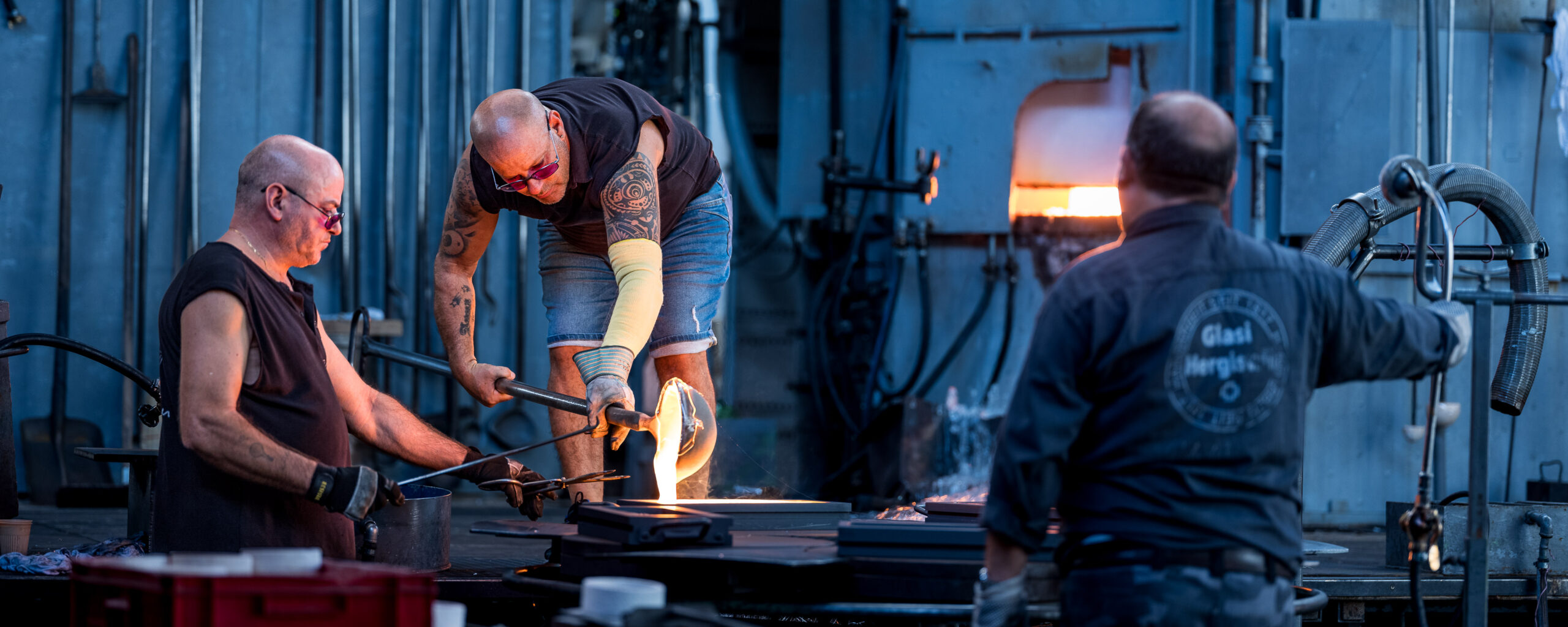 Mehrere Glasmacher arbeiten gemeinsam an glühendem Glas in der Glasi Hergiswil