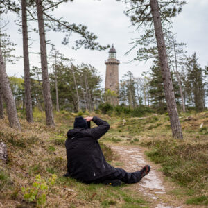 Fotograf sitzend in einem Wald vor einem Leuchturm in Dänemark.