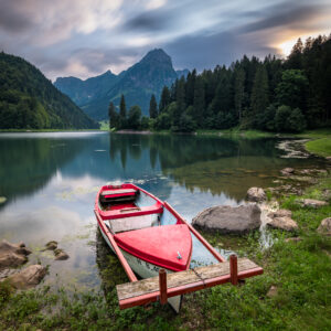 Kleines rotes Boot an einem Unfer und im Hintergrund Wälder und Berge.