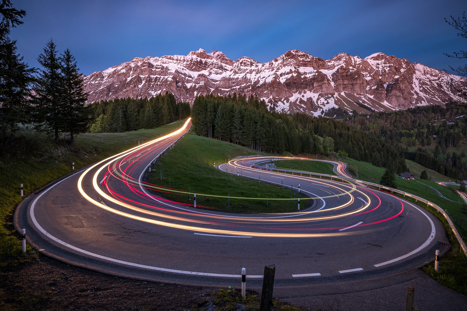 Serpentinenstrasse bei Nacht mit Langzeitbelichtung und leuchtenden Lichtspuren vor schneebedeckten Alpengipfeln – geschwungene Linien und S-Form als Bildgestaltungselemente