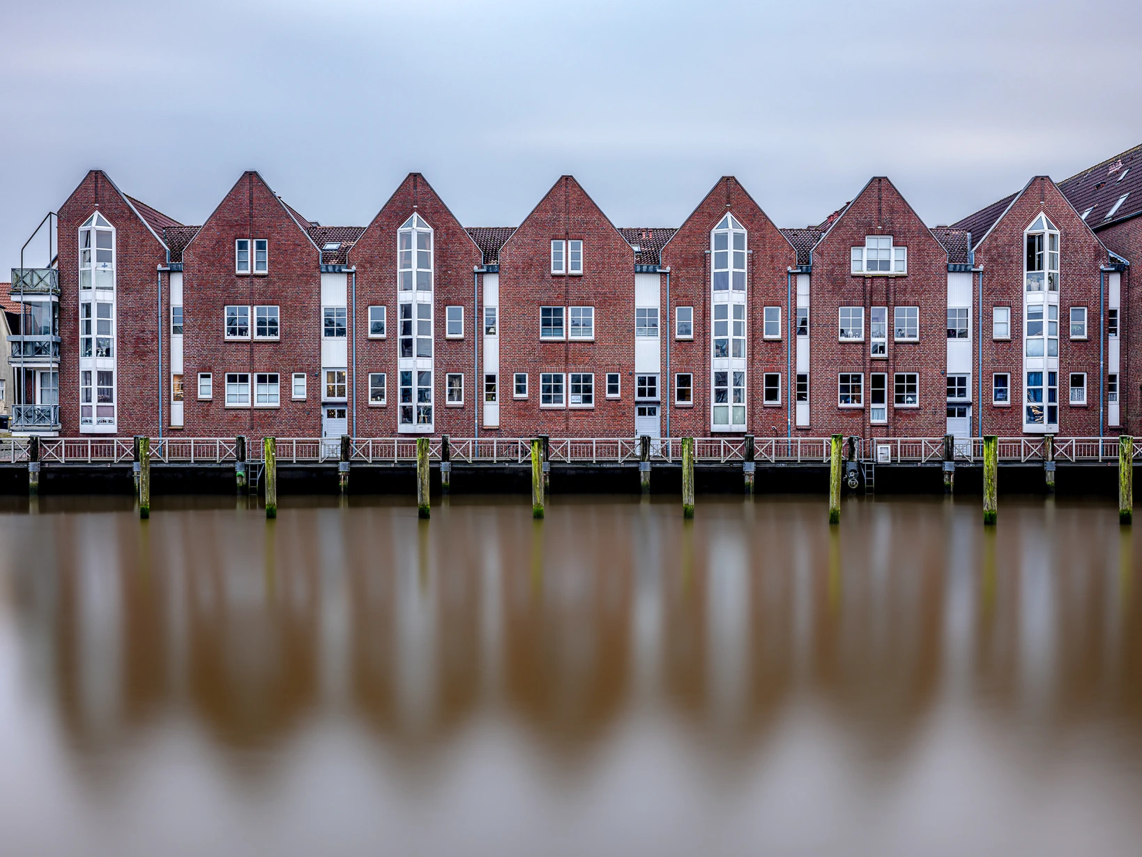 Reihe roter Backsteingebäude am Hafen mit rhythmischer Fassade und glatter Wasseroberfläche durch Langzeitbelichtung – Bildgestaltung durch Wiederholung, Symmetrie und Spiegelung