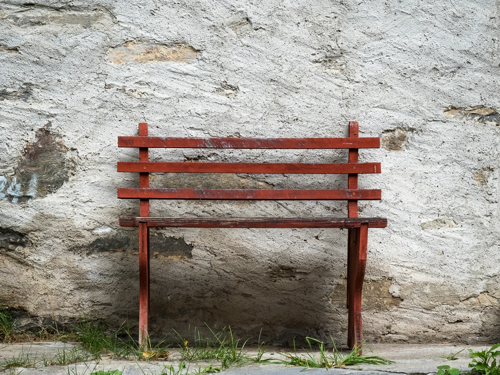Übung minimalistisch fotografieren – rote Holzbank vor grauer Steinmauer, klares Motiv vor gezielt gewähltem Hintergrund