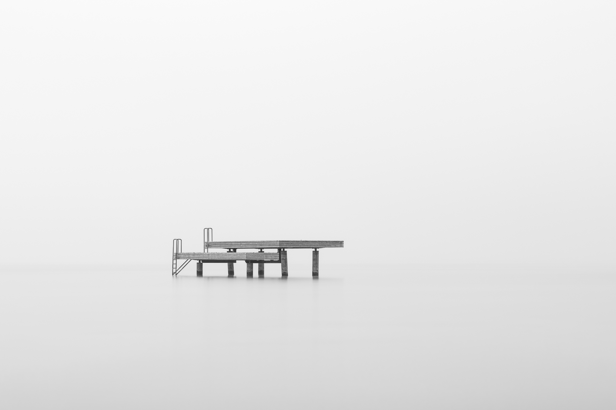 Negativraum in der Fotografie – Badesteg im Nebel, Motiv im unteren Bildbereich, grosser leerer Bildraum gibt dem Steg Gewicht