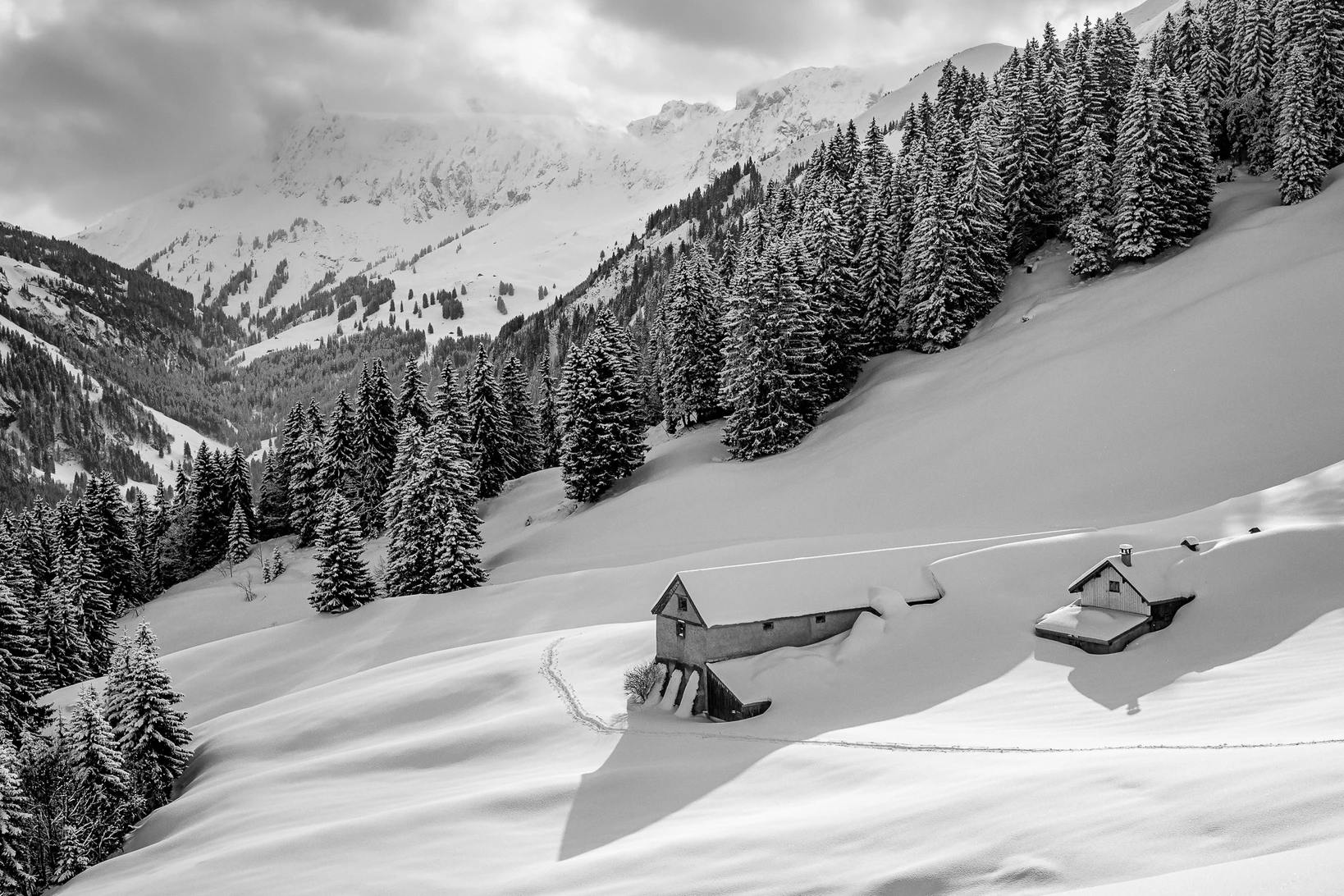 Schwarzweissaufnahme einer verschneiten Alpenlandschaft mit zwei fast eingeschneiten Berghütten und weiten Schneeflächen, weite Flächen als Merkmal ruhiger Bilder