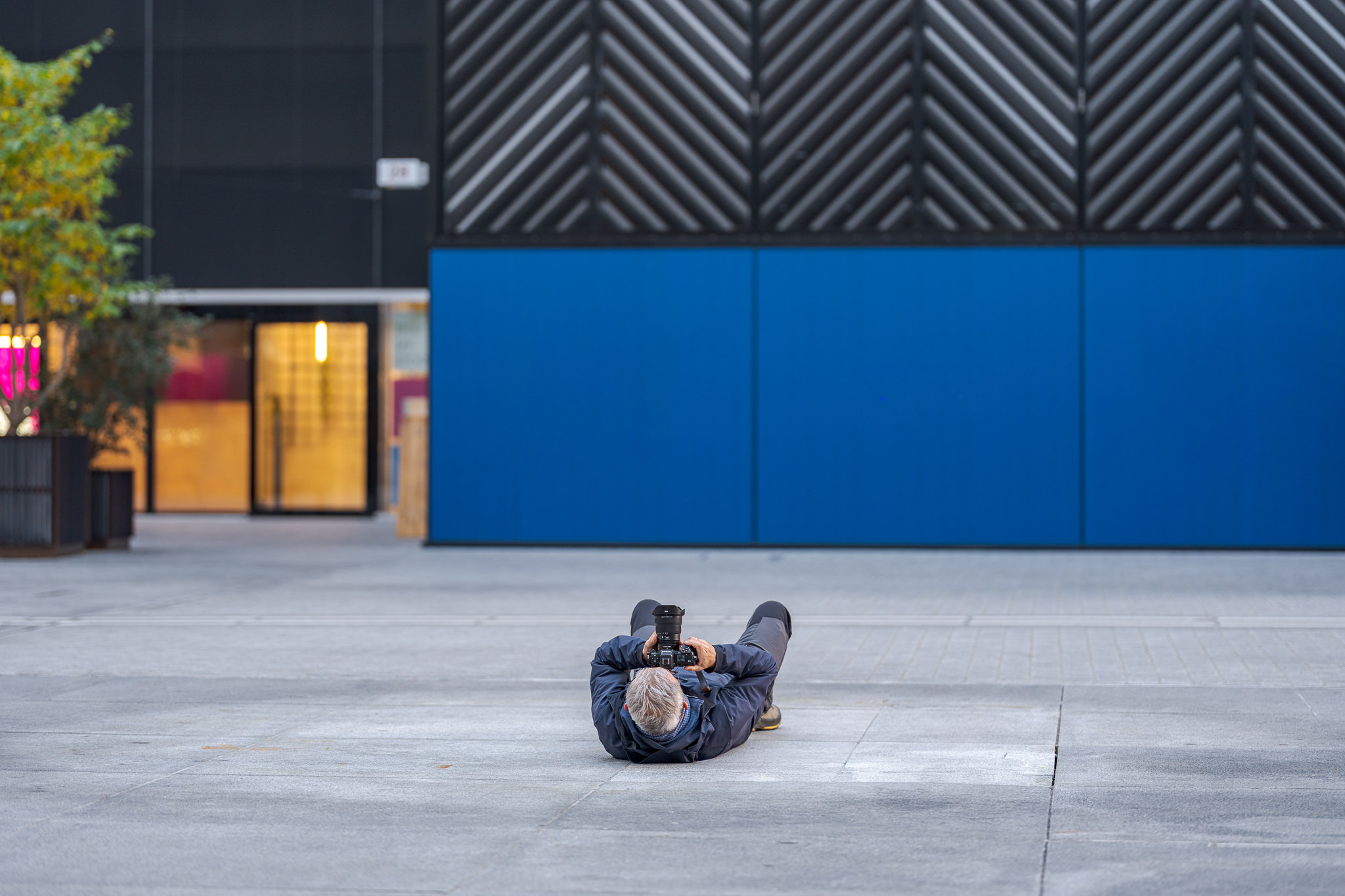 Fotograf liegt flach auf einem Stadtplatz und fotografiert aus der Froschperspektive – Perspektive wechseln als fotografisches Prinzip.