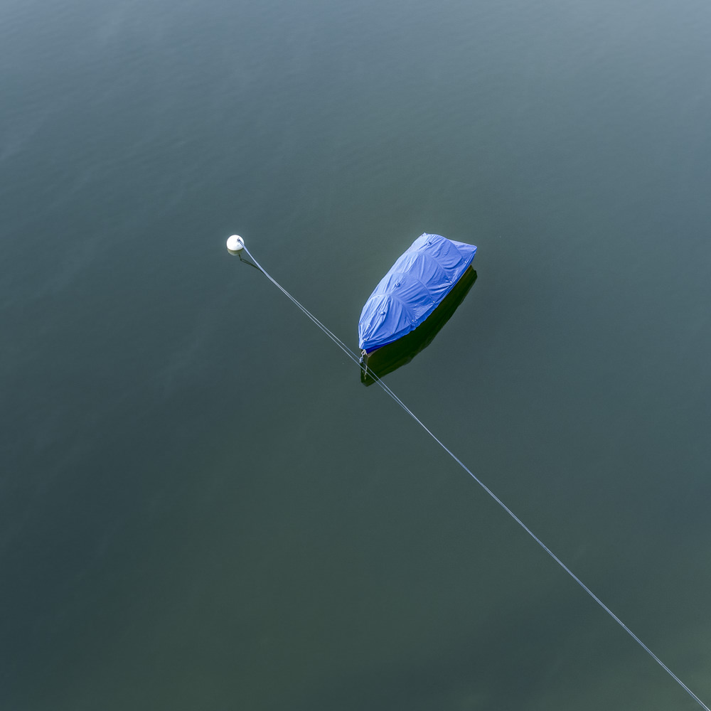 Blau abgedecktes Boot auf ruhigem Wasser mit diagonal verlaufender Ankerleine.