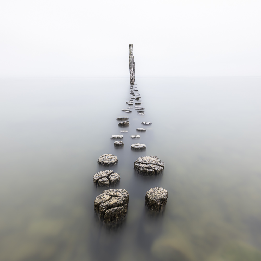Reihe alter Holzpfähle, die durch das ruhige Wasser zu einem einzelnen Pfahl führt.