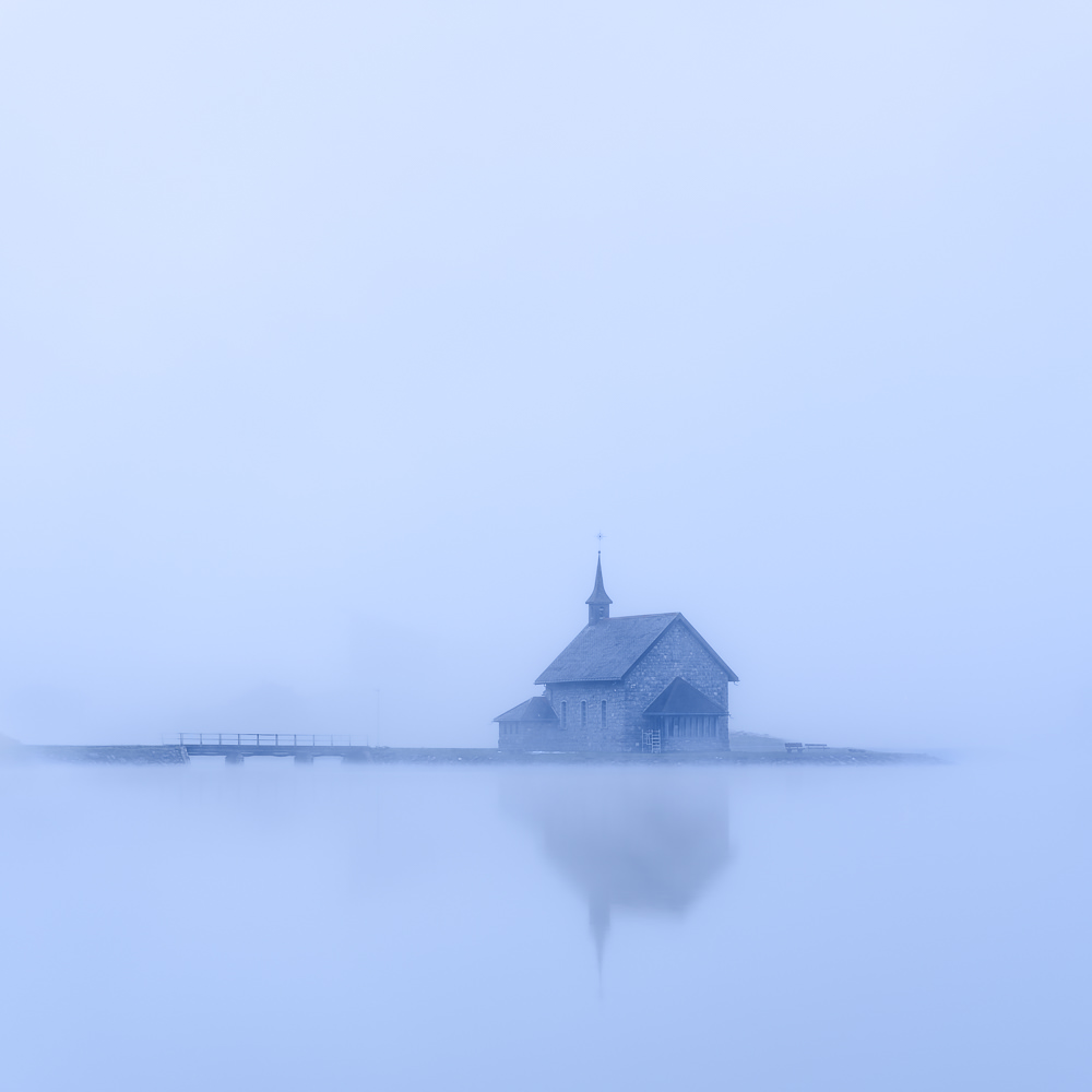 Kirche auf einer kleinen Insel im See, umgeben von dichtem blauem Nebel.