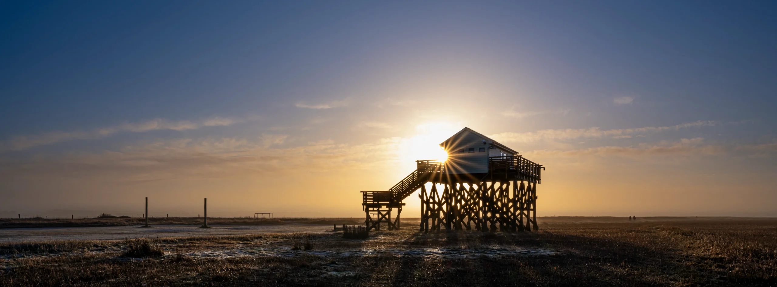 Pfahlbau im Gegenlicht mit Sonnenstern in weiter Landschaft